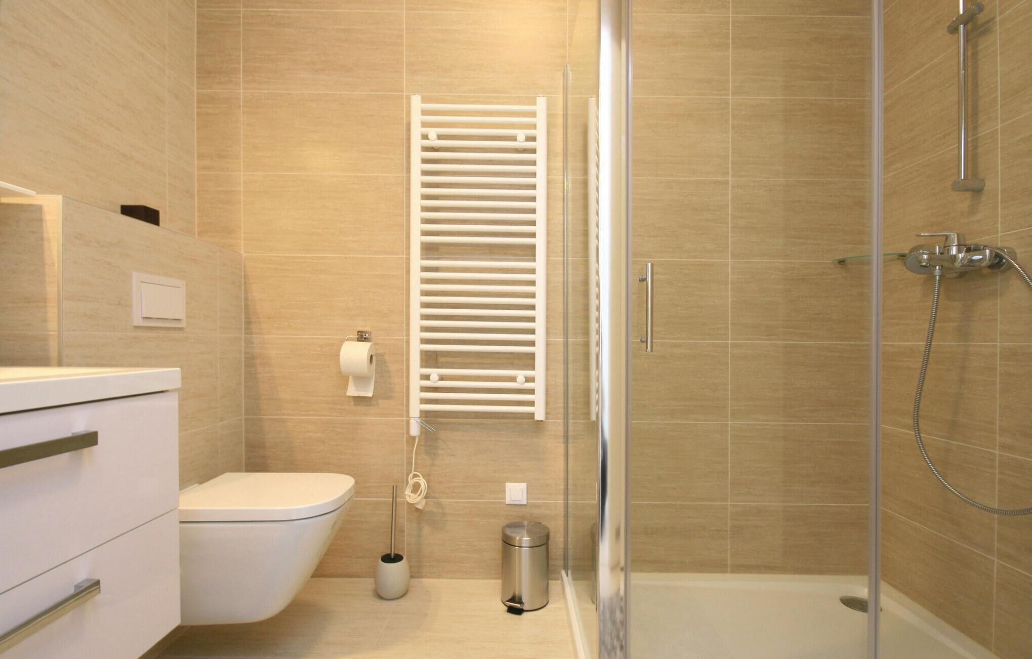 Un baño moderno con inodoro, cabina de ducha de vidrio, toallero y cubo de basura.