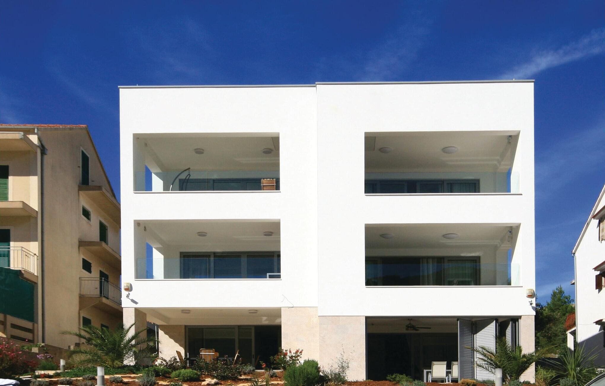 A modern multi-story building with balconies, large windows, and a flat roof.