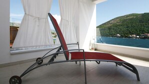 Un balcón con una silla roja, cortinas blancas y vistas al paisaje costero.