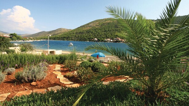 Paisaje costero con vista despejada al mar, un barco y una zona de playa con una sombrilla azul.
