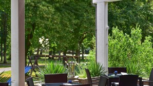 An outdoor patio area with wicker furniture and a view of a park with trees and a wooden fence.