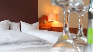 A hotel room with a neatly made bed, a bedside lamp, and a bottle of water.