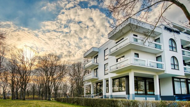 A modern multi-story building with balconies, large windows, and a well-maintained lawn.