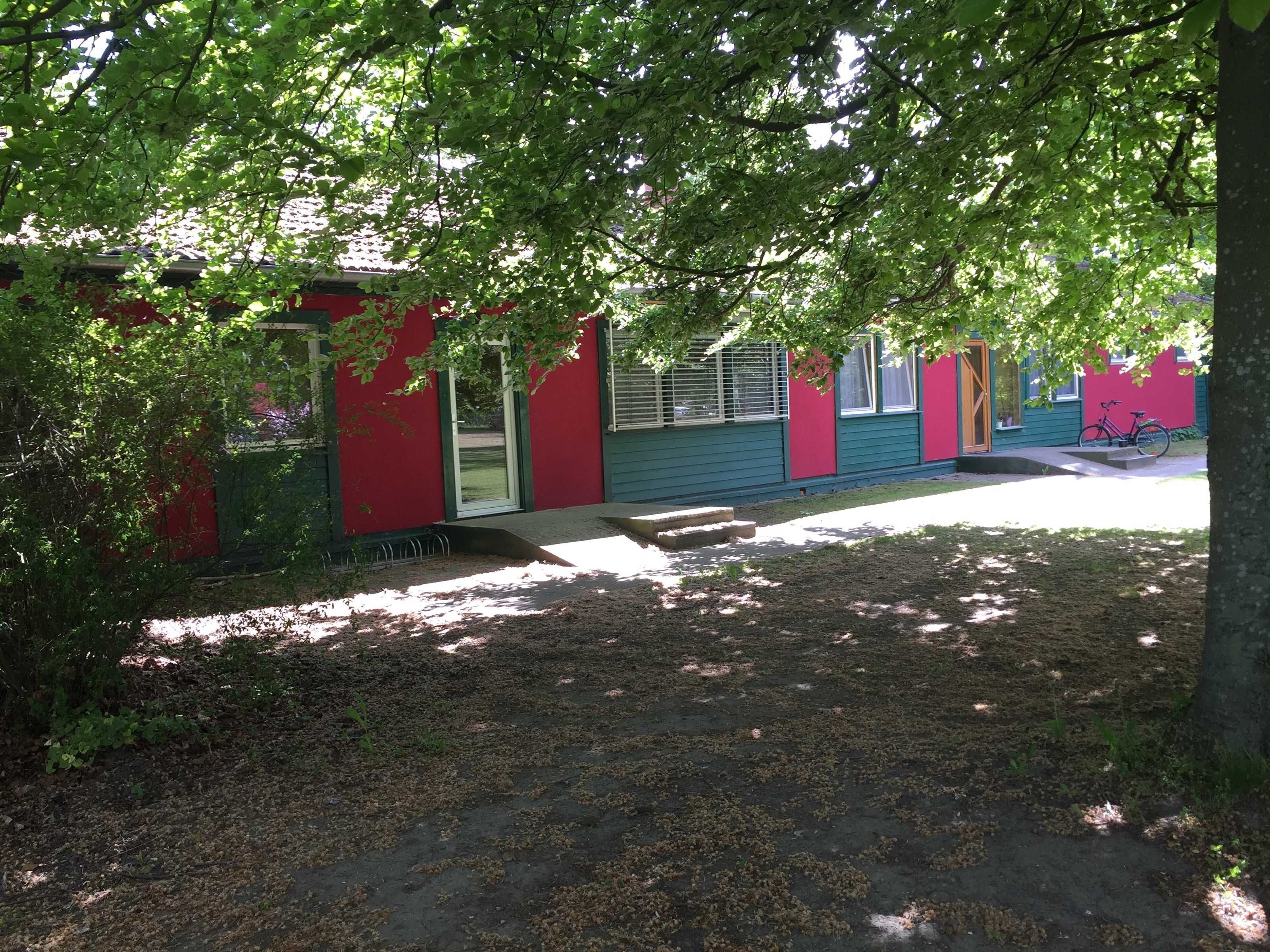 A red and green building with a covered porch and a bicycle parked outside.