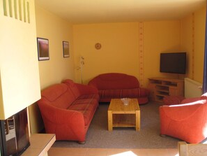 Un salon avec un canapé rouge, une table basse en bois, un téléviseur et un radiateur.
