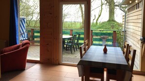 A wooden interior with a dining table and chairs, a red armchair, and a view of a green deck and trees outside. - Windland Ranch - Riding stables with vacation apartments (House 2) - Apartment Seeadler (Altenkirchen)