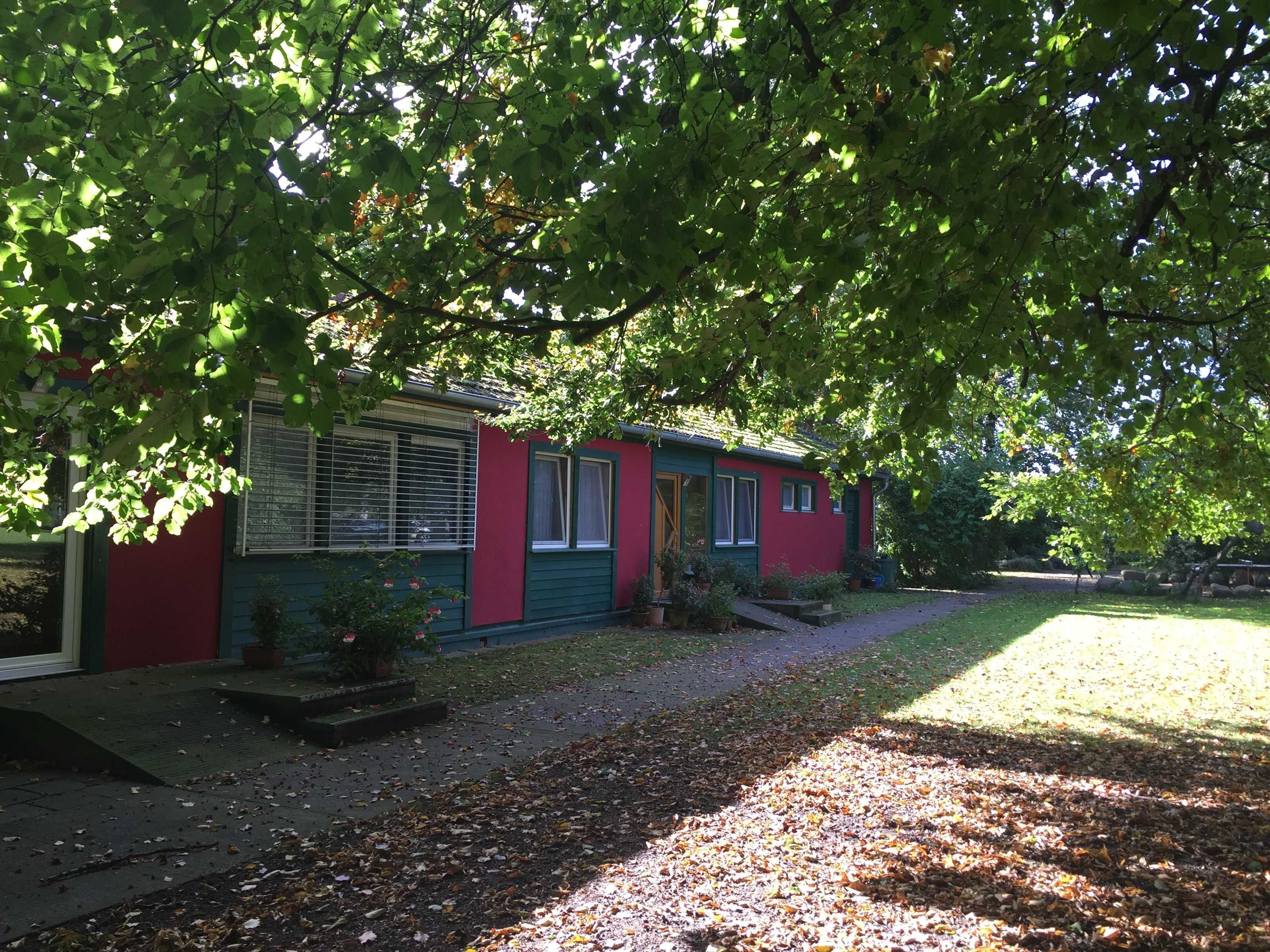 A red and green house with a porch, surrounded by trees and a gravel path.