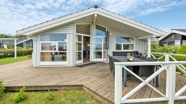 Een modern huis met een houten terras, grote ramen en een overdekte zithoek buiten.