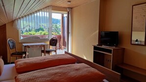 A bedroom with a bed, a television, a chair, and a window with a view of greenery. - Double Room with Balcony 1 - Gasthaus Zum Pälterwald (Oberzent)