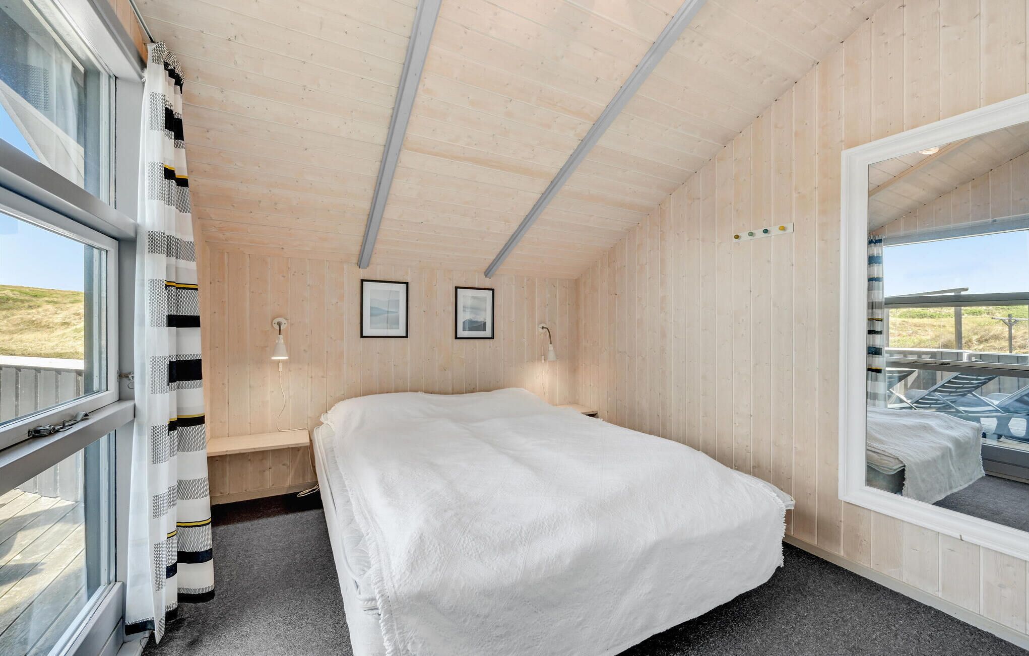A cozy cabin room with a bed, wooden walls, and a large window offering a view of the outdoors.