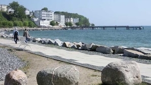 Une promenade en bord de mer, avec de gros rochers, une jetée et des bâtiments en arrière-plan.