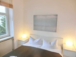 Habitación de hotel con cama, dos mesitas de noche con lámparas, ventana con persianas y un cuadro en la pared.