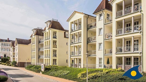 Een rij meergezinswoningen met balkons, een heldere lucht en een straat op de voorgrond.