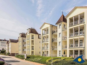 Una fila di edifici residenziali a più piani con balconi, cielo sereno e una bandiera nell'angolo.