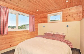 Quarto com cama, duas janelas, vista exterior e uma pequena janela sobre a cama.