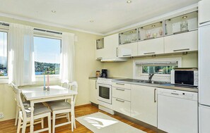A modern kitchen with white cabinetry, a dining table with chairs, a view of the sea through the window, and a built-in oven and microwave. - Cozy apartment in Straumsgrend (Straumsgrend)