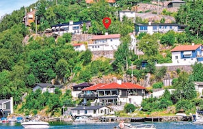 A coastal village with houses on a hillside, a marina with boats, and a red location marker. - Cozy apartment in Straumsgrend (Straumsgrend)