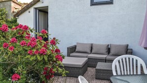 Un patio con un sofá de mimbre, cojines, una silla blanca y una mesa.