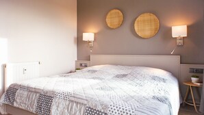 A neatly made bed with a patterned quilt, two wall-mounted lamps, and two woven wall decorations. - (166) 2-room apartment - apartment complex Yachthafenresidenz (Kühlungsborn)