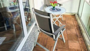A balcony with a glass door, a folding chair, a small round table with a vase of flowers, and a wooden floor. - (166) 2-room apartment - apartment complex Yachthafenresidenz (Kühlungsborn)