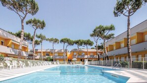 Ein Swimmingpool, umgeben von weißen Liegestühlen und Bäumen, mit gelben Gebäuden im Hintergrund.