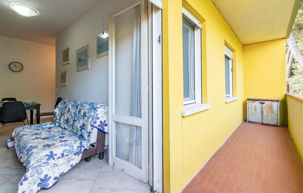 Ein Zimmer mit Bett, Tisch, Stühlen und einem Fenster mit Vorhängen, sowie einer gelben Wand.