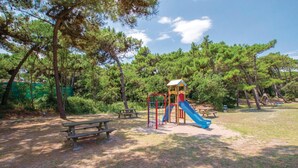 Ein Spielplatz mit Rutsche und Klettergerüst, umgeben von Bäumen und Picknicktischen.