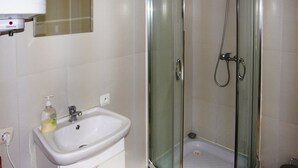 Un bagno con un lavandino bianco, una doccia vetrata e uno specchio sopra il lavandino.