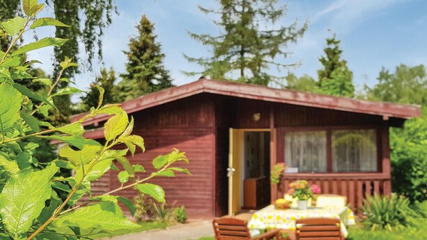 Una baita di legno con un portico, un tavolo e sedie, e un giardino di fronte.