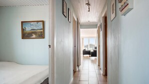 A narrow hallway with a bed on the left, a dining area in the center, and a kitchen visible through an open door at the end.