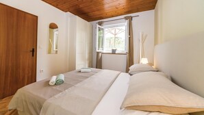 A bedroom with two beds, wooden ceiling, a window with curtains, and a bedside lamp.