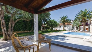 A covered outdoor area with a pool, wicker furniture, and a view of a building with a tiled roof.