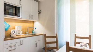 Cocina compacta con microondas, cafetera y lavabo. Hay sillas de madera y una mesita con una vela.