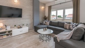 A modern living room with a grey sofa, a white coffee table, and a flat-screen TV mounted on a brick wall. - Gorgeous apartment in Biograd with WiFi (Biograd)