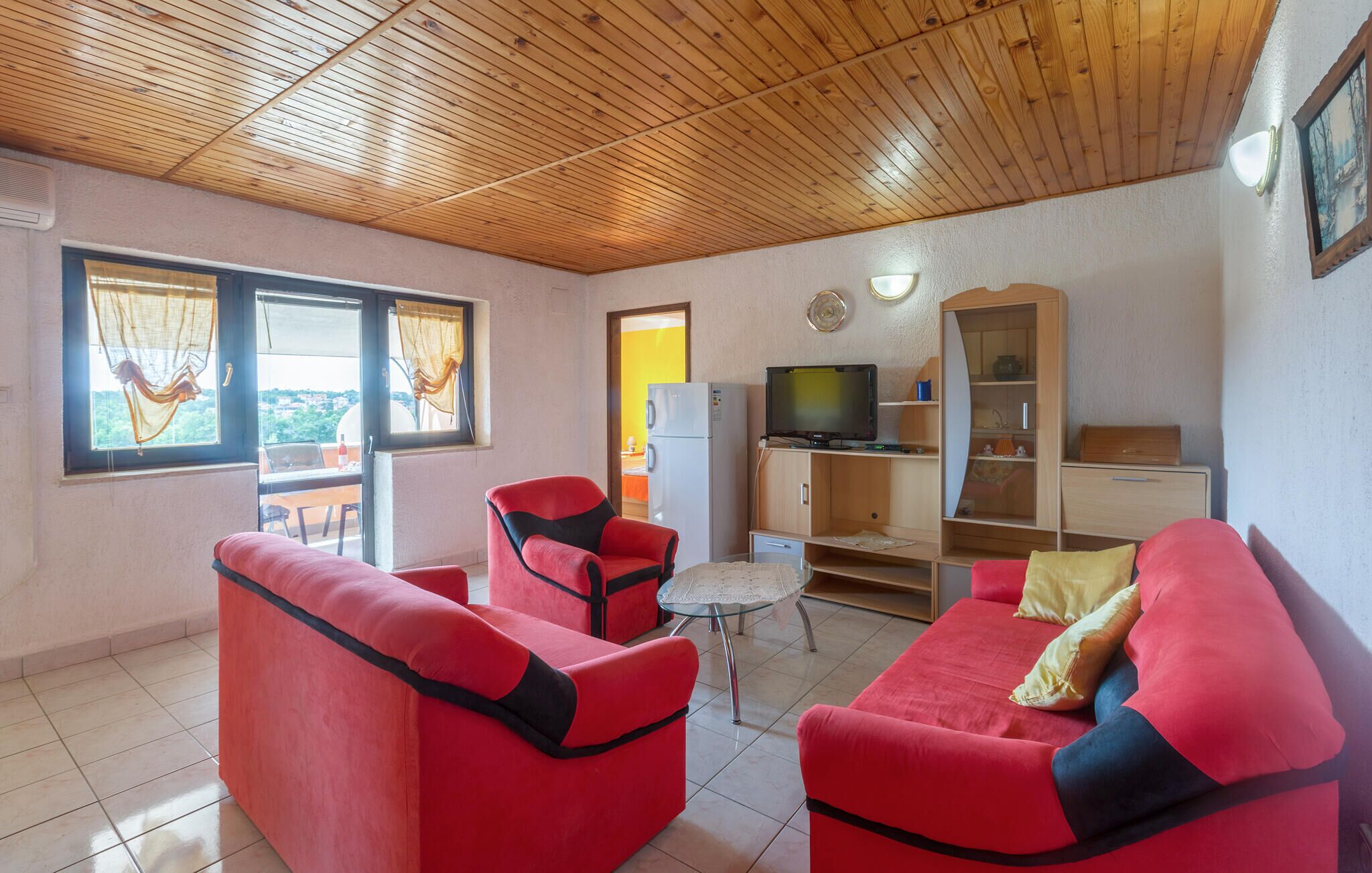 A cozy living room with red sofas, a television, and a wooden ceiling.