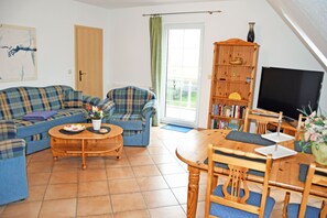 A living room with a sofa set, a coffee table, a dining table with chairs, a bookshelf, and a television.