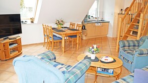 Ein gemütliches Wohnzimmer mit Fernseher, einem Esstisch mit Stühlen, einer Couch und einer Küchenzeile mit Holdekor und einer Treppe.