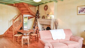A cozy living room with a staircase, a fireplace, a pink sofa, and a dining area with wooden furniture. - Nice home in Landreville with kitchen (Landreville)