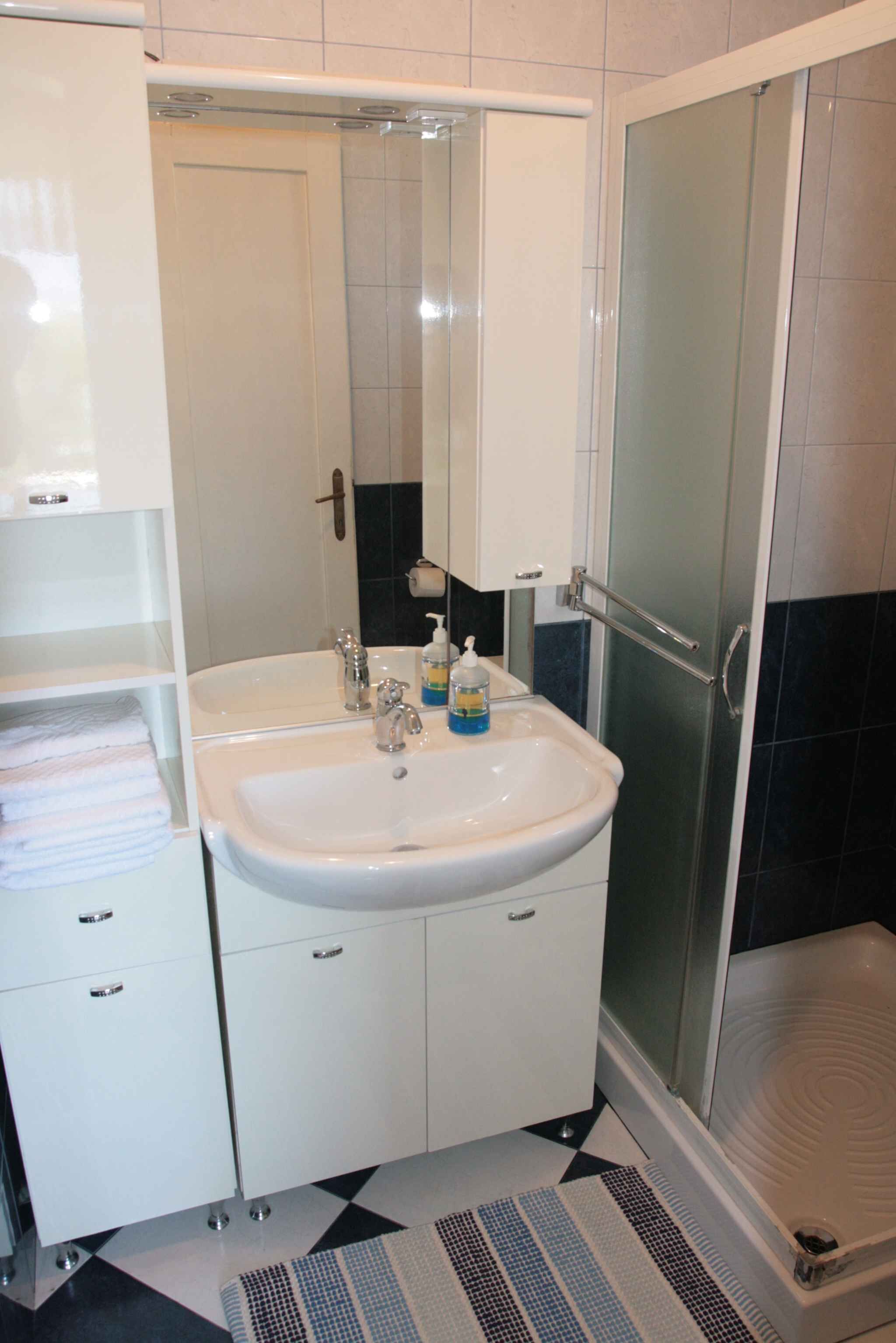 A bathroom with a white sink, mirror, and shower enclosure.