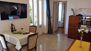 Ein Essbereich mit Tisch für zwei Personen, einem an der Wand befestigten Fernseher und einer Holzvitrine mit Büchern.