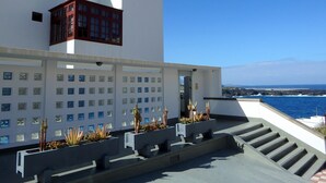 A modern building with a white facade, a red structure on the left, and a view of the ocean.
