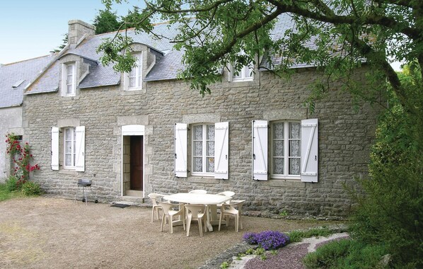 Una casa de piedra con un patio de grava, una mesa de madera y sillas.