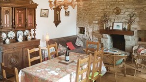 Ein gemütliches Wohnzimmer mit Kamin aus Stein, Holzmöbeln und einem Essbereich mit blumigem Tischläufer.
