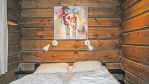 Een houten kamer met een bed, twee bedlampen en een kleurrijk abstract schilderij aan de muur.