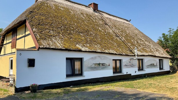 Ett traditionellt hus med halmtak, en väggmålning, en skorsten och siffran 9 på väggen.