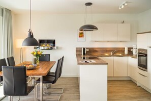 Uma cozinha moderna com armários brancos, uma ilha de madeira e uma luminária pendente preta.