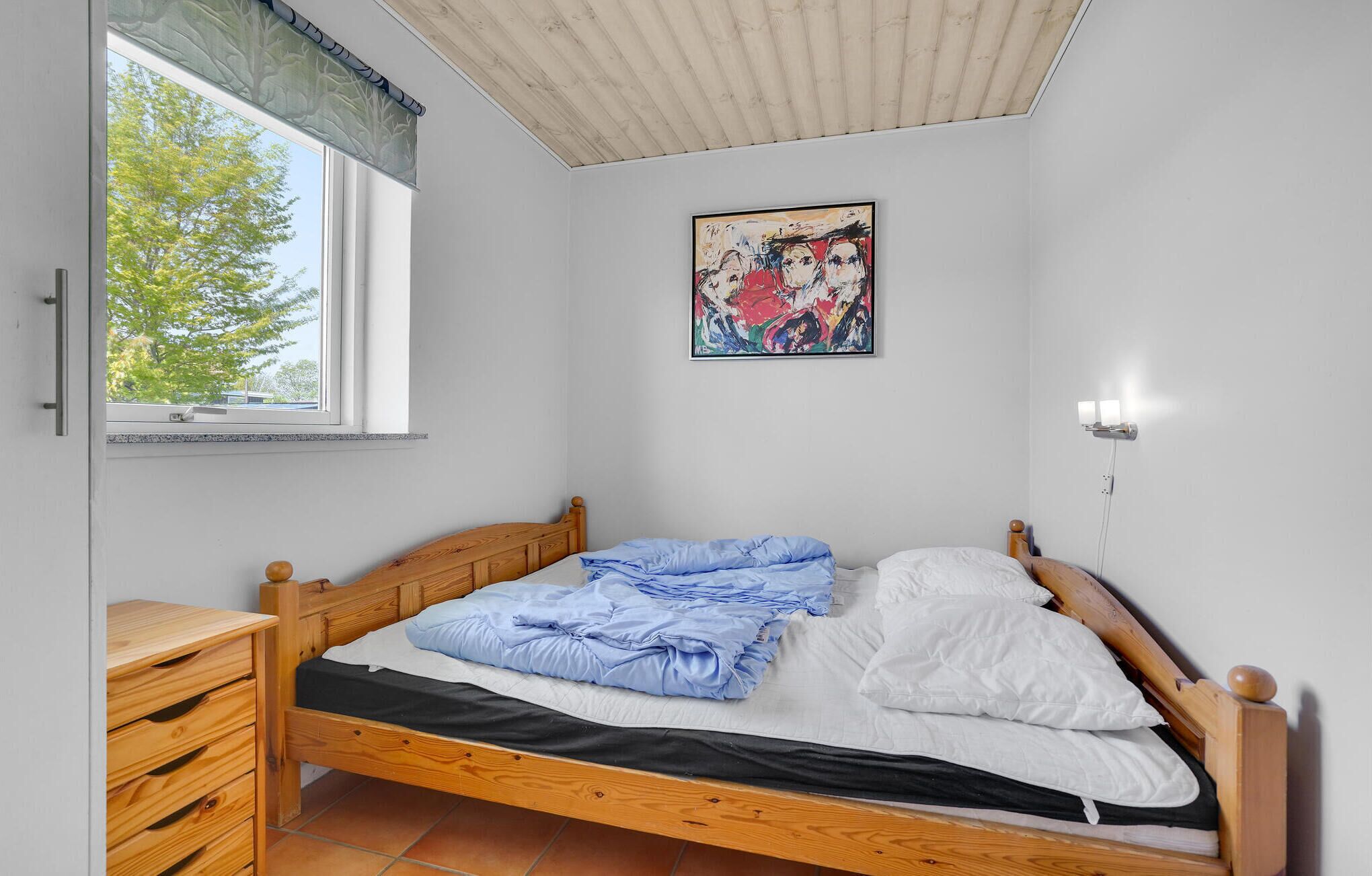Ein Schlafzimmer mit einem hölzernen Bett, einem Fenster mit Blick auf Bäume, einem an der Wand hängenden Gemälde und einem Nachttisch.