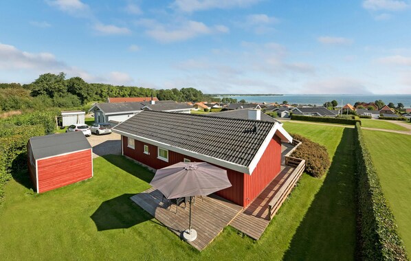 A red building with a tiled roof, a covered patio, and a view of the sea. - Stunning home in Sjølund with kitchen (Sjølund)