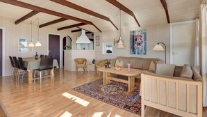 A spacious living area with a wooden floor, a sofa, a dining table with chairs, and a kitchen area in the background. - Stunning home in Sjølund with kitchen (Sjølund)