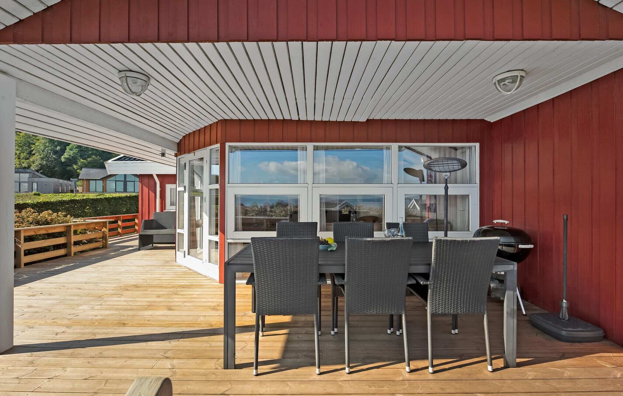 A covered outdoor dining area with a table and chairs, large windows, and a view of the surrounding landscape.